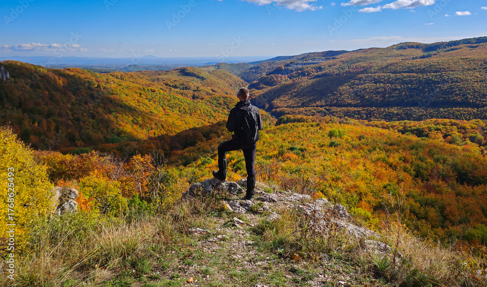 Obraz premium A hiker stands on the edge of Köpüs-kő in the Bükk Mountains, gazing over the colorful autumn forests and valleys of northern Hungary.