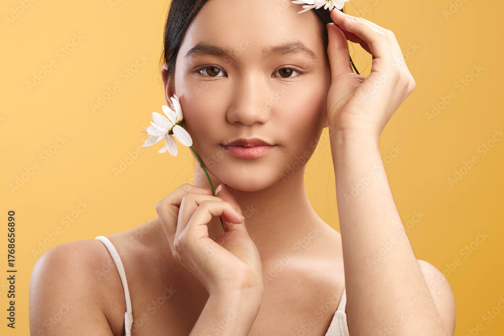 Ταπετσαρία asian woman gazes softly at the camera, holding white flowers near her face against a warm background, conveying natural beauty, calm charm, and gentle elegance