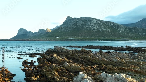 Rocky coastal landscape with turquoise sea and mountain range under soft evening light creating a cinematic natural scenery
