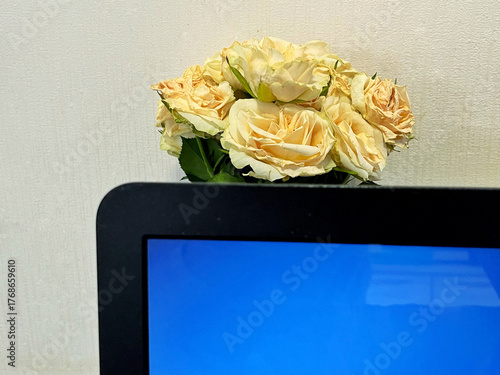 Computer monitor with blue screen and a bouquet of soft yellow roses in a glass vase, creating a serene workspace atmosphere with floral elements enhancing the environment