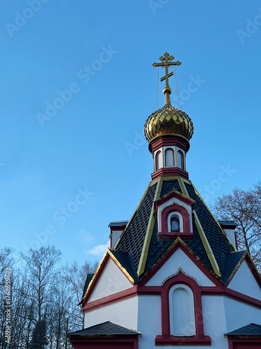 Colorful church features a striking golden dome and cross, set against a backdrop of trees and blue sky, highlighting architectural beauty and cultural heritage