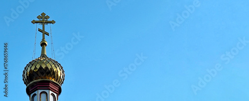 Golden domed church tower with intricate cross against a clear blue sky, showcasing architectural beauty and religious symbolism in a serene environment