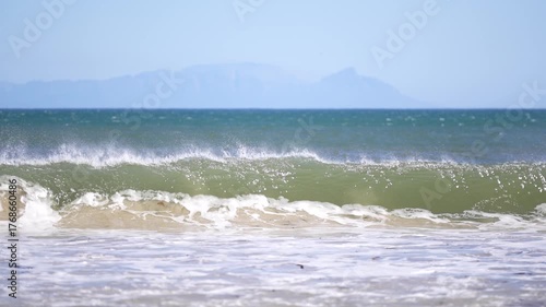 Powerful ocean wave crashing on shore with bright sea spray and clear blue horizon creating a fresh natural and cinematic seascape mood
