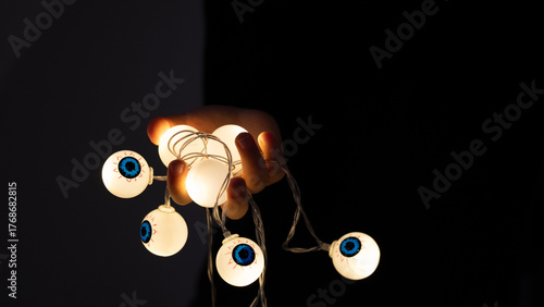 Hand holding glowing eyeball Halloween lights on dark background