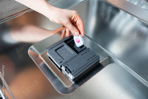 Hand inserts dishwasher detergent tablet into dispenser - tablet, detergent, dishwasher, clean, cycle.