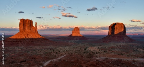 Landscape of Monument Valley in Arizona at sunset, showing the East Mitten Butte, West Mitten Butte, and the Merrick Butte