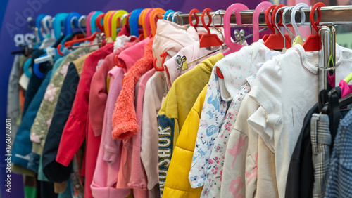 Colorful children's clothes hanging on a rack at a sustainable swap event. Various jackets, sweaters, and shirts in bright colors symbolize reuse, recycling, and eco-friendly fashion for kids.