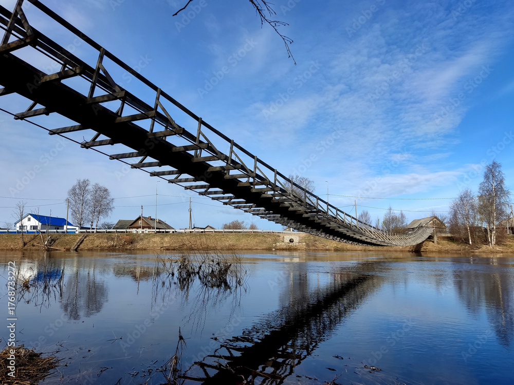 Fototapeta premium A wooden suspension bridge in the village of Verkhovye, Olonetsky District, Republic of Karelia, Russia, spanning the Olonka River.
