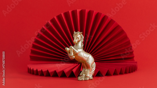 Golden horse figurine with red paper fan background. Symbol of 2026 — the Year of the Fire Horse in the Chinese zodiac. Represents strength, energy, and prosperity