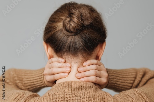 Woman massaging neck pain from behind showing tension in nape area on neutral background