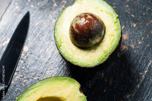 ripe avocado cut in half on a dark stone textured surface.