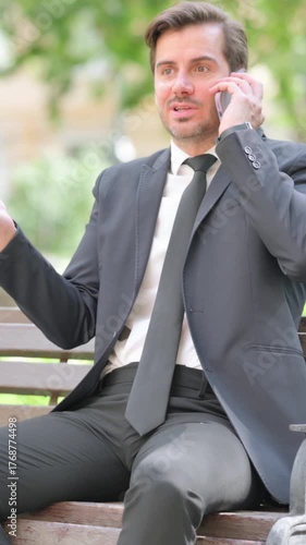 Angry Middle Aged Businessman Talking on Phone while Sitting Outdoor