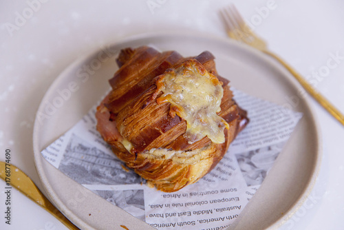 Savory croissant filled with melted cheese and smoked ham, golden flaky layers with cheese oozing, served on ceramic plate with paper liner