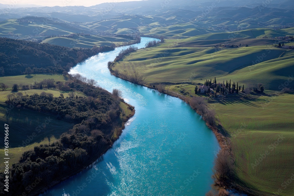 Fototapeta premium Aerial view showcases a winding river flowing through rolling green hills under soft, diffused
