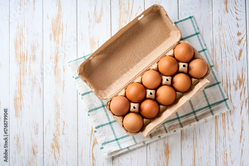 chicken eggs in a carton box on a light kitchen table, selective focus, top view.