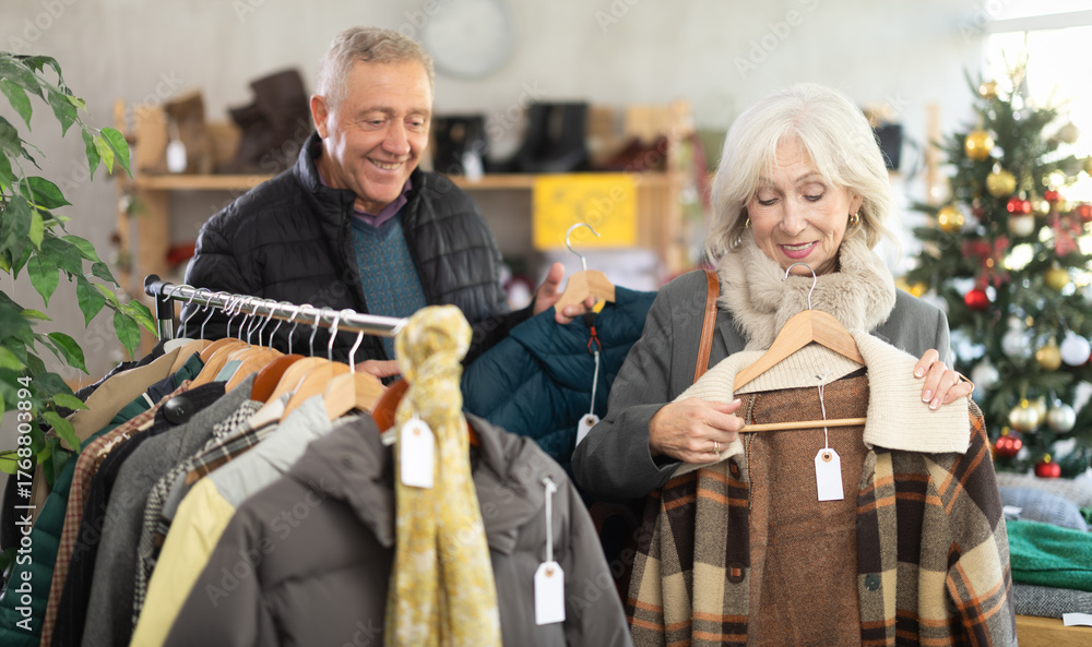 Fototapeta premium Glad old-aged spouses looking for winter outwear in retail outlet during X-mas sell-out season
