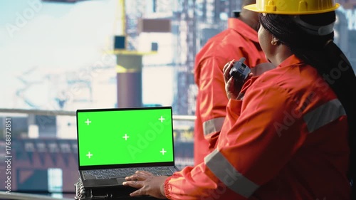 Isolated screen laptop used by energy production company worker to determine optimal drilling rig locations. Woman on offshore platform ship looking at well sites data on mockup notebook, camera B