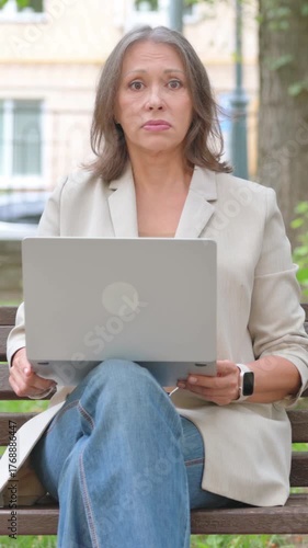 Shocked Old Senior Woman Looking at Camera while Using Laptop in Park