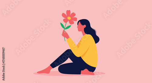 A peaceful woman sits on the floor, admiring and gently smelling a vibrant red and yellow flower, finding joy in simple pleasures.