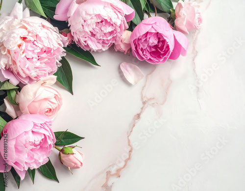Beautiful pink peonies with green leaves arranged on a light marble background, creating an elegant floral composition.