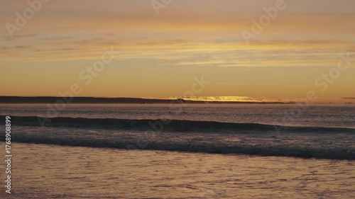 Serene dawn over Playa Las Canteras beach in Puerto Madryn, Argentina, with golden sun and calm ocean waves.