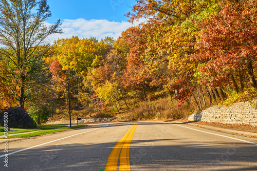 Country road with yellow line going down the middle and colorful fall leaves on a pretty autumn day