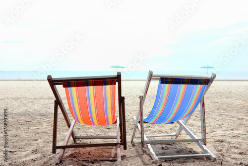 Two chairs are placed on the sandy beach, overlooking the clear sky and sea.