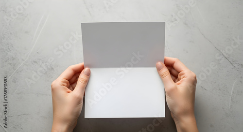 Hands holding an open blank greeting card on a gray surface.