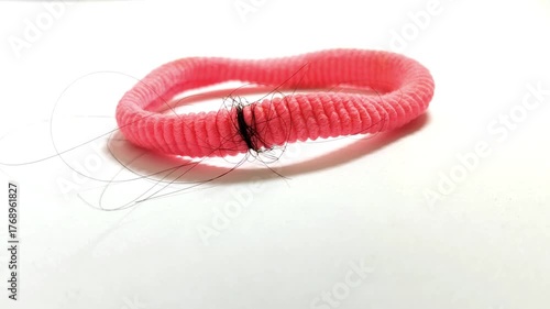 Closeup of a pink hair tie on a white background, with strands of hair wrapped around it. Hair care or hair loss concept