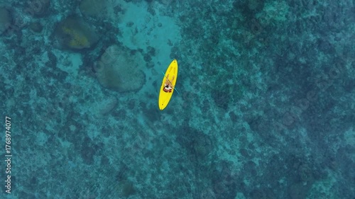aerial view  woman bright yellow kayak with  in the vast expanse of crystal clear turquoise water. The seabeds rocky texture is visible beneath the surface, concept marine environment.