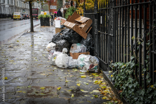 Stack of garbage bags and cardboard boxes on a rainy urban street. Waste management, pollution, and environmental issues
