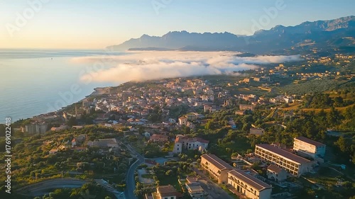 Coastal town nestled in hills near sea with misty mountains.