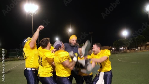 Football team lifting and throwing their coach in the air, celebrating a win on the field at night