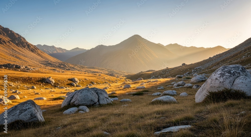Fototapeta premium Sunny mountain valley scene with rocks, dry grass, and peak bathed in golden light