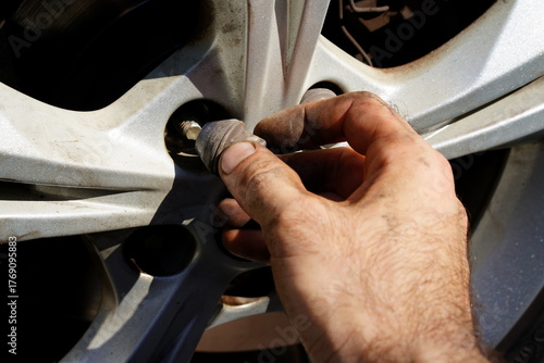 Hand tightening a wheel bolt on a silver car in a garage during daylight