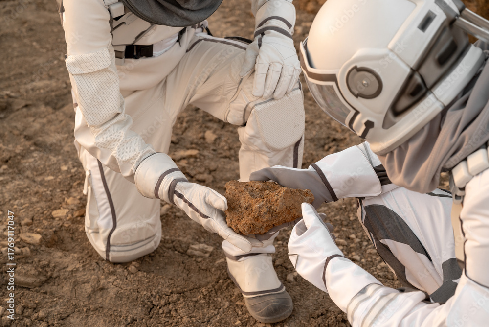 Fototapeta premium Explorers in astronaut suits holding and observing alien ground samples on the red planet.