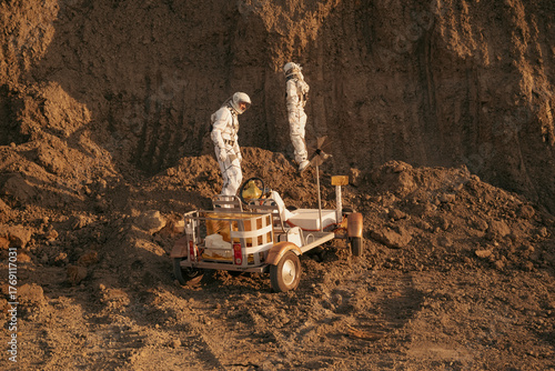 Astronauts conducting geological study beside red rock formation and rover