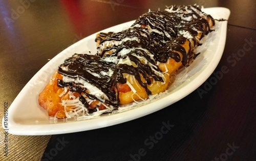 fried bananas with chocolate and cheese topping on a leaf-shaped plate