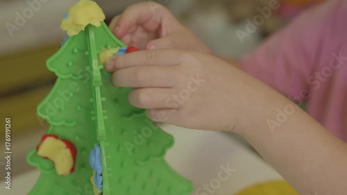  Girl is making Christmas tree decorations out of clay for a plastic Christmas tree
