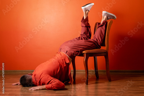 Fatigued man in orange suit suffering burnout falling on chair indoors