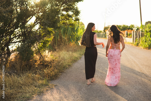 Two close friends are taking a leisurely walk together at sunset along a beautiful scenic road