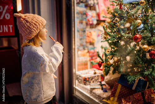 Child admires festive window display adorned with Christmas decorations