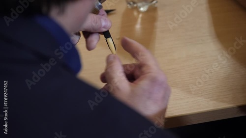 Hands shaping oboe reed with reed knife on wooden bench