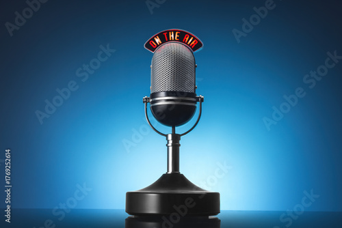 A vintage silver microphone on a stand against a blue studio backdrop.Radio, podcasting, voiceovers, broadcasting with a professional retro