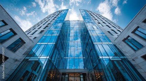 Modern architectural structure features curved glass facade reflecting bright blue sky with scattered clouds