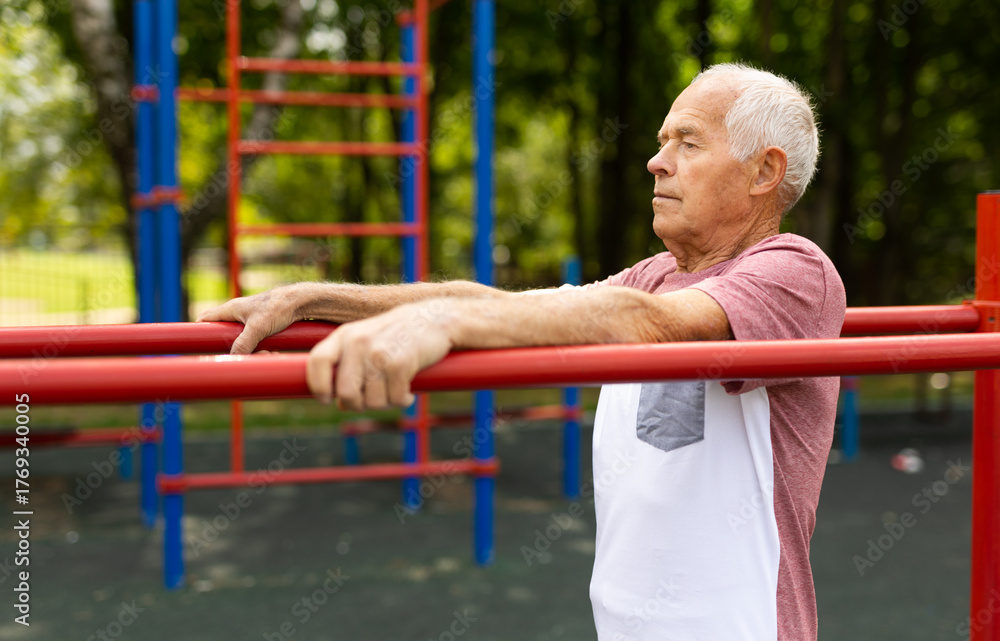 Obraz premium Senior man performing parallel bar exercises in park