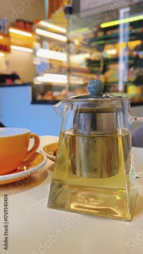 A yellow teacup and transparent teapot with tea on table in cafe. Vertical video. Blurred background. High quality 4k footage