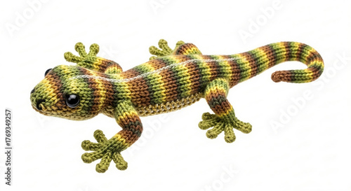 A small, knitted gecko toy with a camo-like stripe pattern in green, brown, and yellow is shown with black safety eyes.