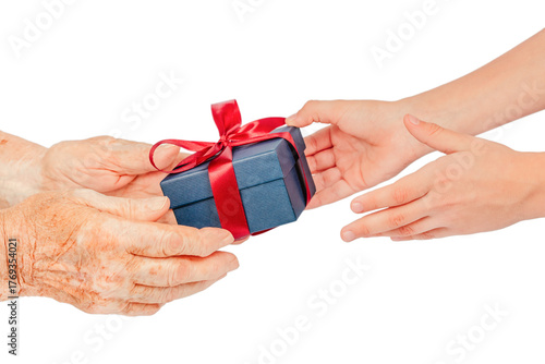 Close-up of elderly and young hands exchanging a blue gift box with a red ribbon, isolated on white. Symbolic concept of giving, care, gratitude, connection, family love between generations.