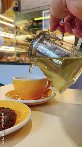 A woman holds teapot and pours tea into yellow cup. Coffee shop interior. Blurred background. Vertical view. High quality 4k footage